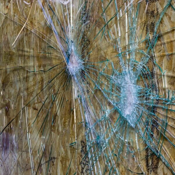 Two severe impact points on a shattered window that has been boarded up with wood, showing failed security against smash and grab crime.