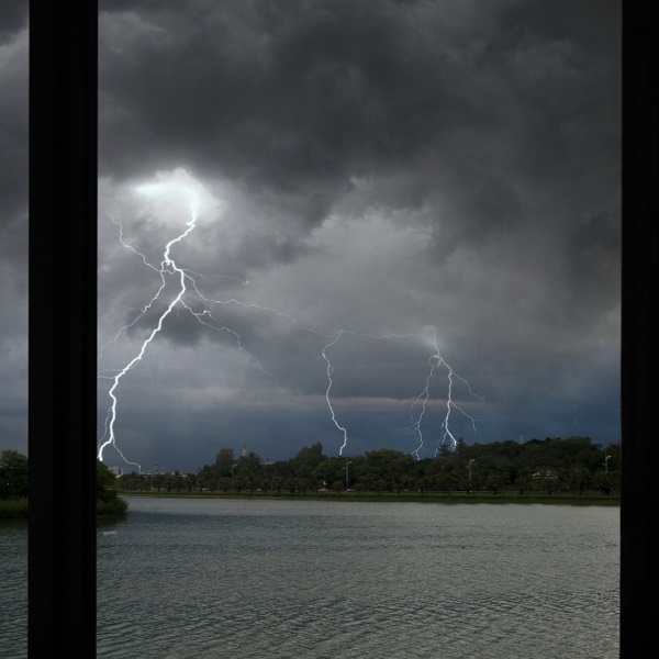 Multiple lightning strikes over a body of water under dark storm clouds, representing the severe weather threats to unprotected windows.