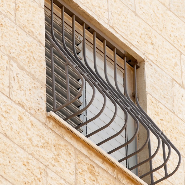 Curved metal security bars installed over a window on a stone building, representing one traditional method for creating a burglar-proof window.