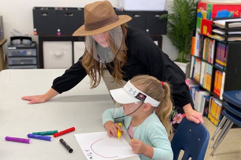A child and a teacher wearing protective face shields for schools.