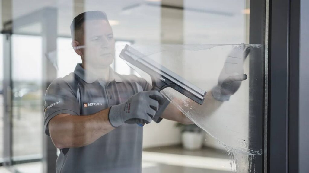 A professional installer is using a squeegee to carefully remove air bubbles during the application of security window film on glass windows. This installation process enhances safety by holding shattered glass in place, providing added protection against break-ins and harmful UV rays.